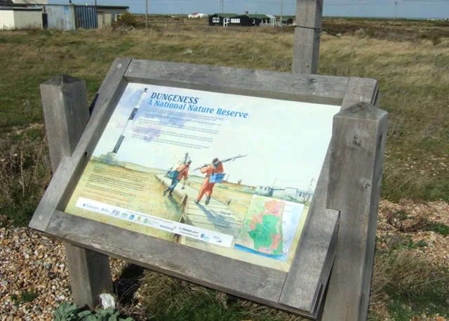 Dungeness National Nature Reserve sign beside shingle ridges and scattered houses