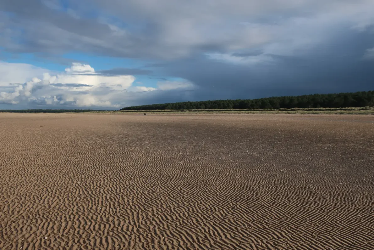 Broad sand and shallow tidal water beneath cloud at Holkham Beach