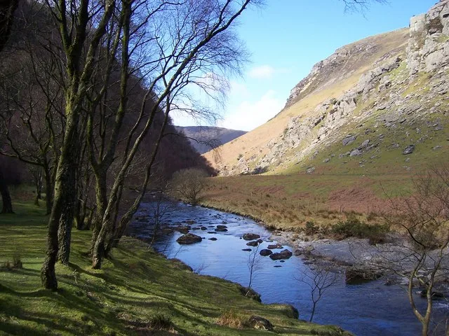 Rock-strewn river beneath leafless riverside trees at Gwenffrwd-Dinas, with a steep hillside beyond